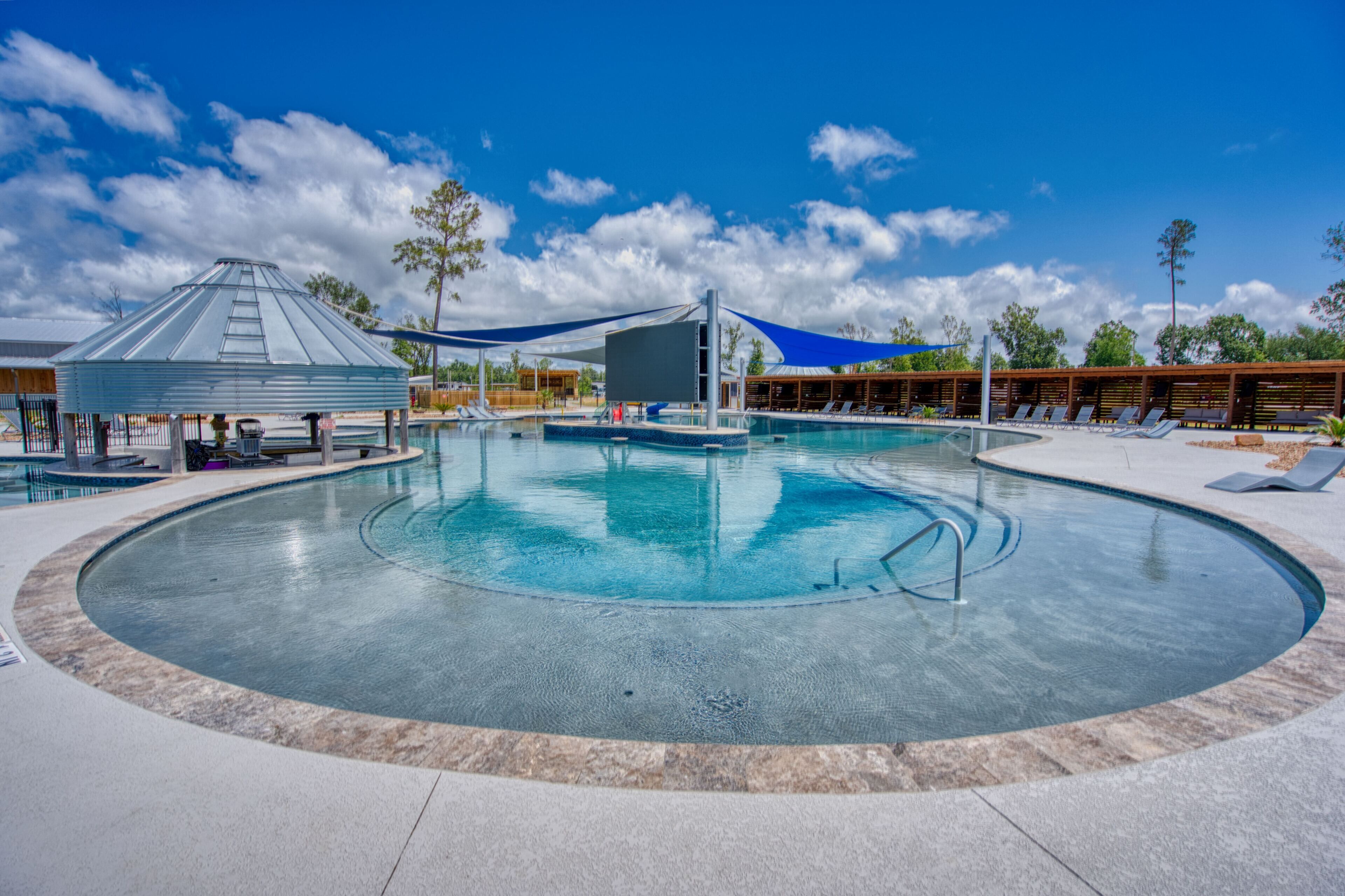 A large outdoor swimming pool with a circular design, surrounded by lounge chairs and shaded areas.
