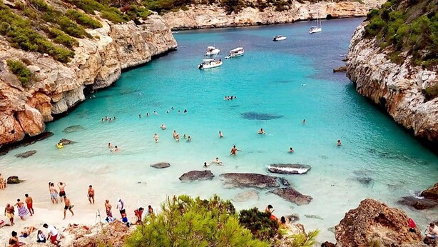 A coastal area with clear turquoise waters, rocky cliffs, and boats.