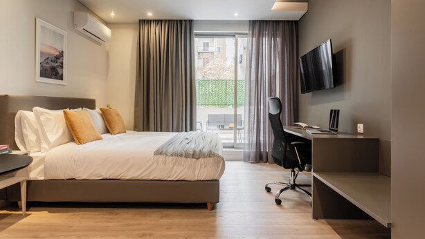 A modern bedroom with a bed, desk, and TV. - WYZ Museum by UPSTREET (Athens)