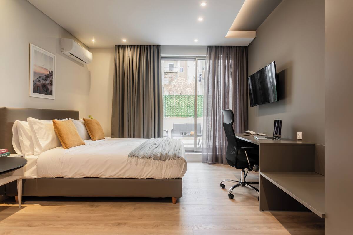 A modern bedroom with a bed, desk, and TV.