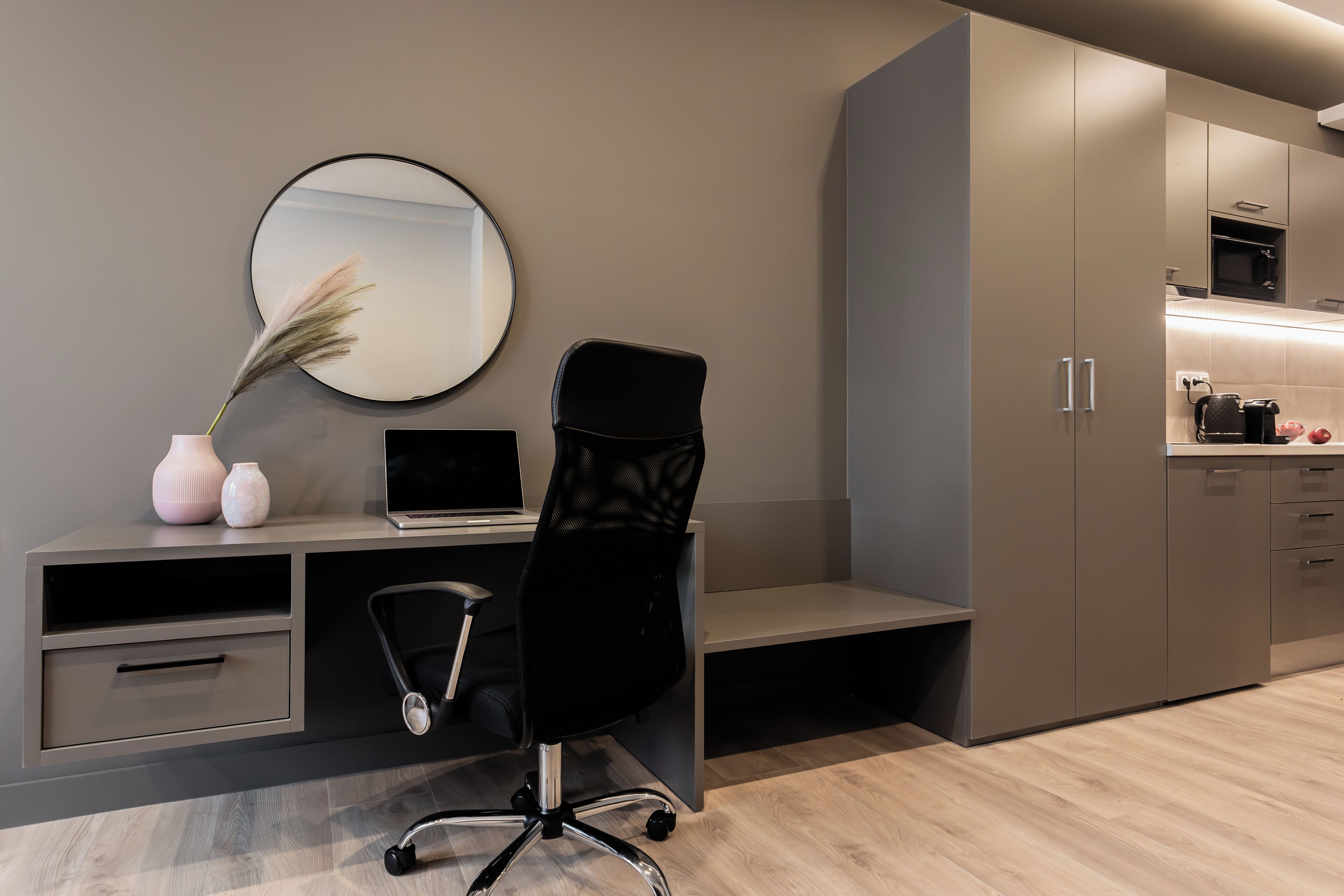 A modern kitchen with grey cabinets, a black chair, and a round mirror on the wall.