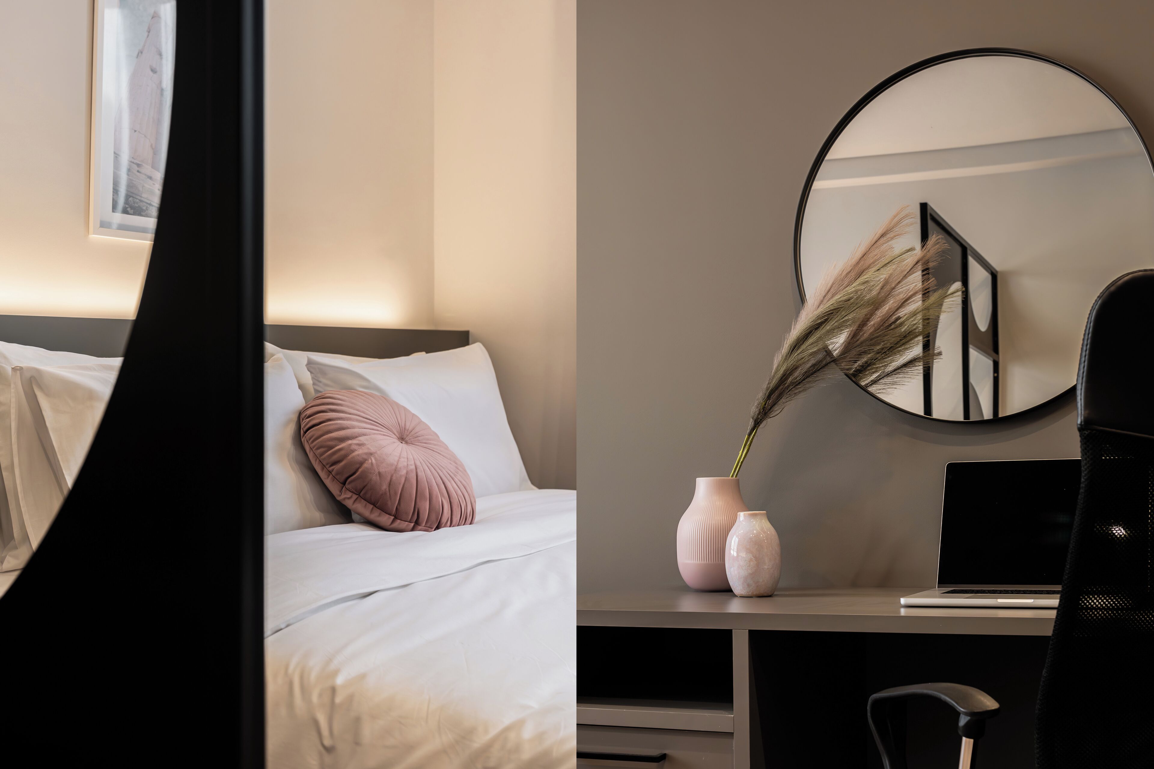 A neatly arranged bedroom with a bed, a bedside table with a laptop, and a mirror reflecting part of the room.