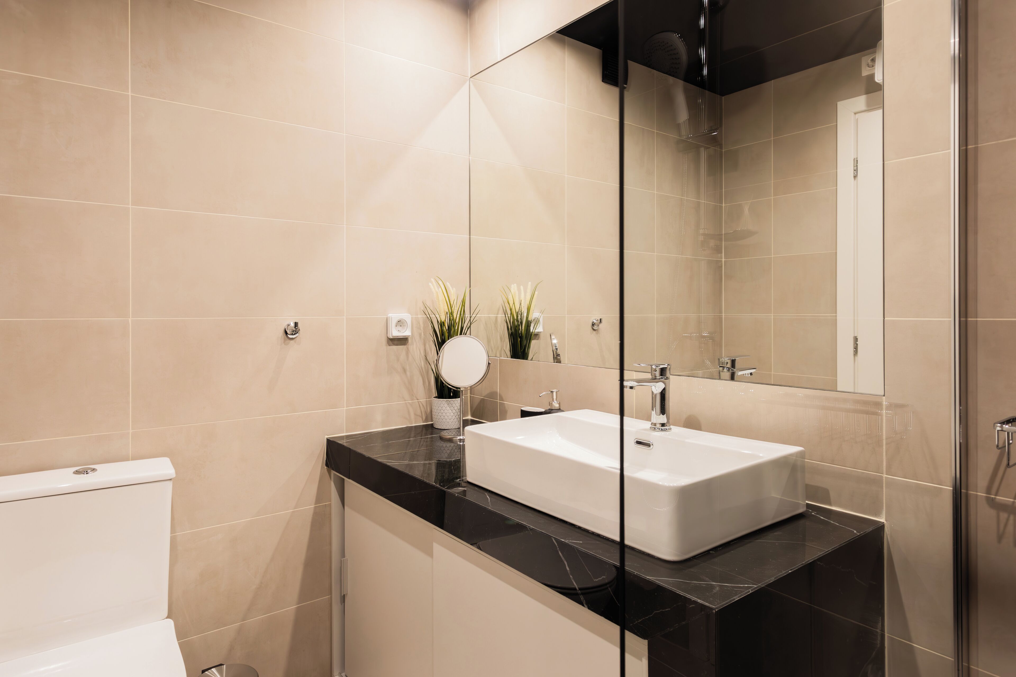 A modern bathroom with a white sink, black countertop, and beige tiles.