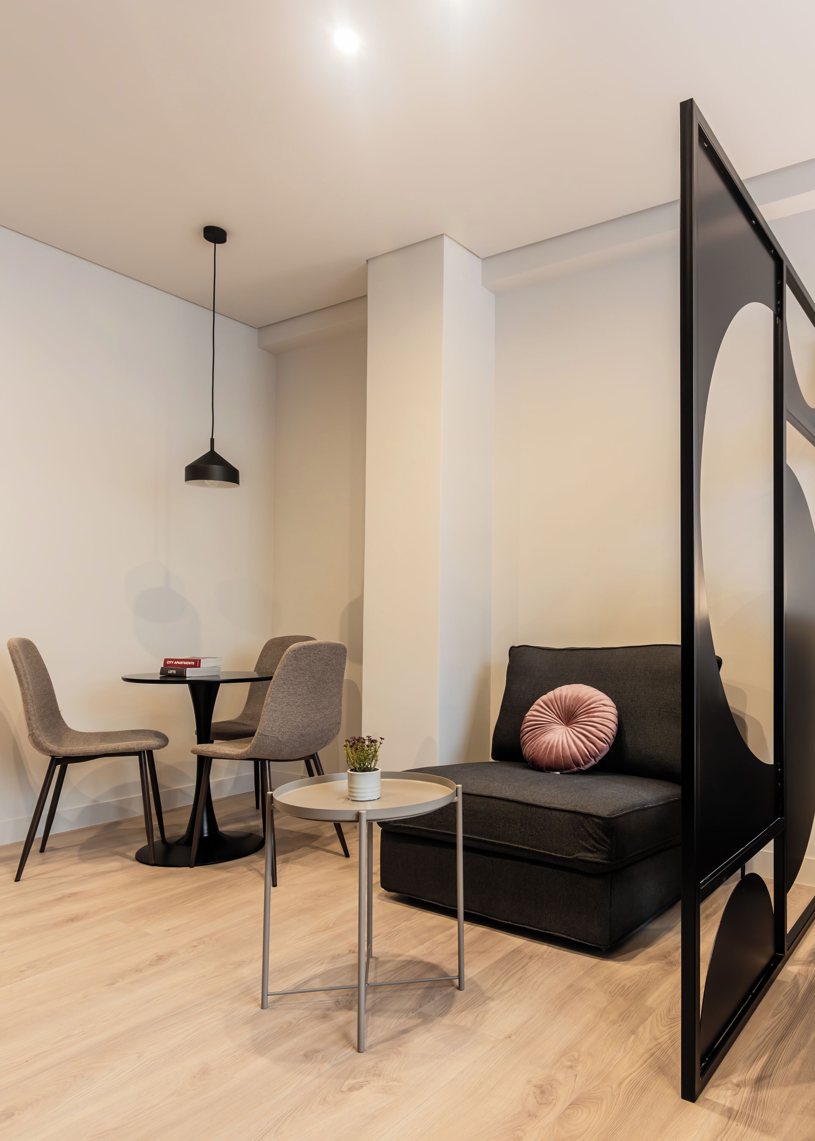 En moderne stue med en sort sofa, grå lænestole, et lille rundt bord og en sort hængende lampe.