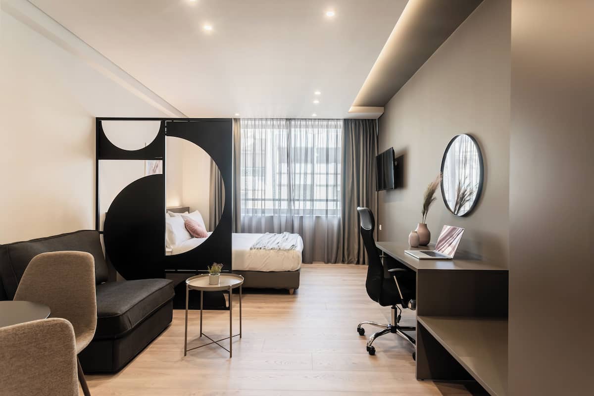 A modern hotel room with a bed, a sofa, a desk, and a small table.