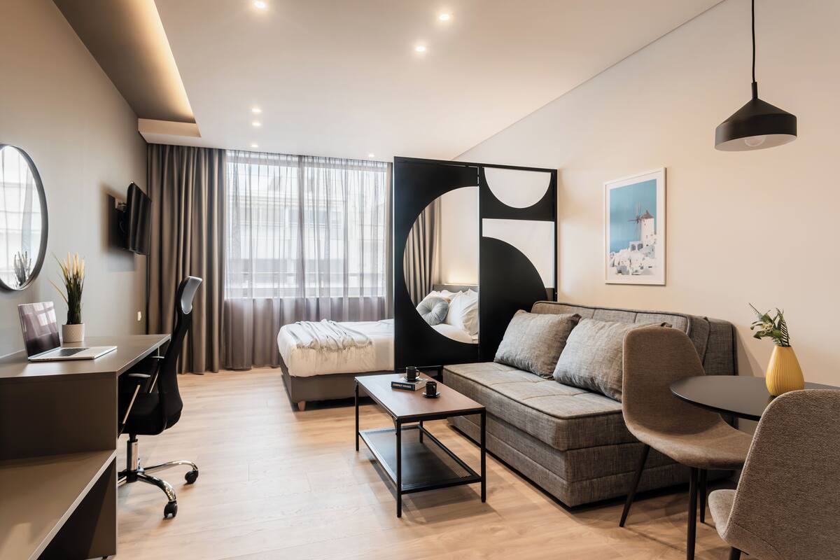 A modern hotel room with a bed, a sofa, a desk, and a dining area.