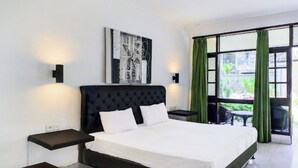 A modern hotel room with a large bed, a nightstand, a wall-mounted light, and a window with green curtains. - Anna Kuta Inn Hotel (Kuta)