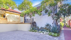 A courtyard with a paved walkway, a small garden with various plants, and a building with a tiled roof. - Anna Kuta Inn Hotel (Kuta)