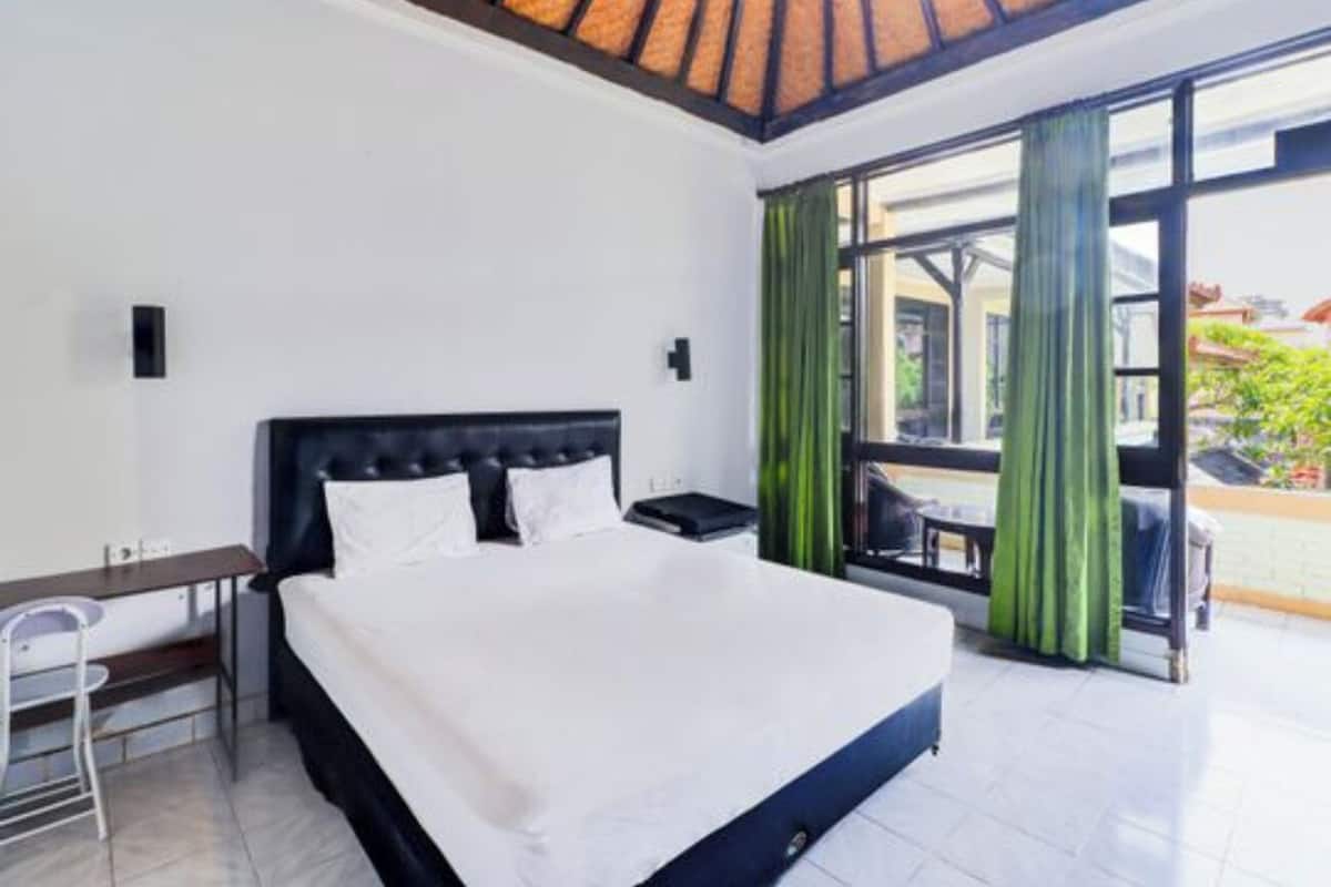 A hotel room with a large bed, a desk, and a view of the outdoors through a glass door.