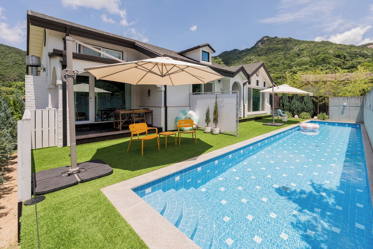 A modern house with a swimming pool, outdoor furniture, and a view of a mountainous landscape.