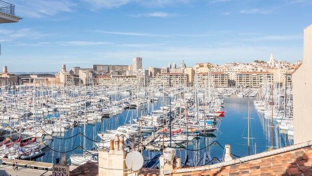A marina with numerous boats docked, a clear sky, and buildings in the background.