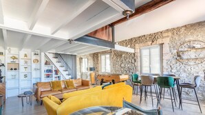 A spacious living area with a yellow sofa, a dining table with chairs, a staircase, and a stone wall.
