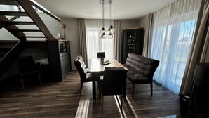 Un salon moderne avec un coin repas, comprenant un escalier, un canapé, une table à manger avec des chaises et un lustre.