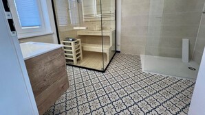 Une salle de bain moderne avec une douche à l’italienne en verre, des carreaux de sol à motifs et un meuble-lavabo en bois.