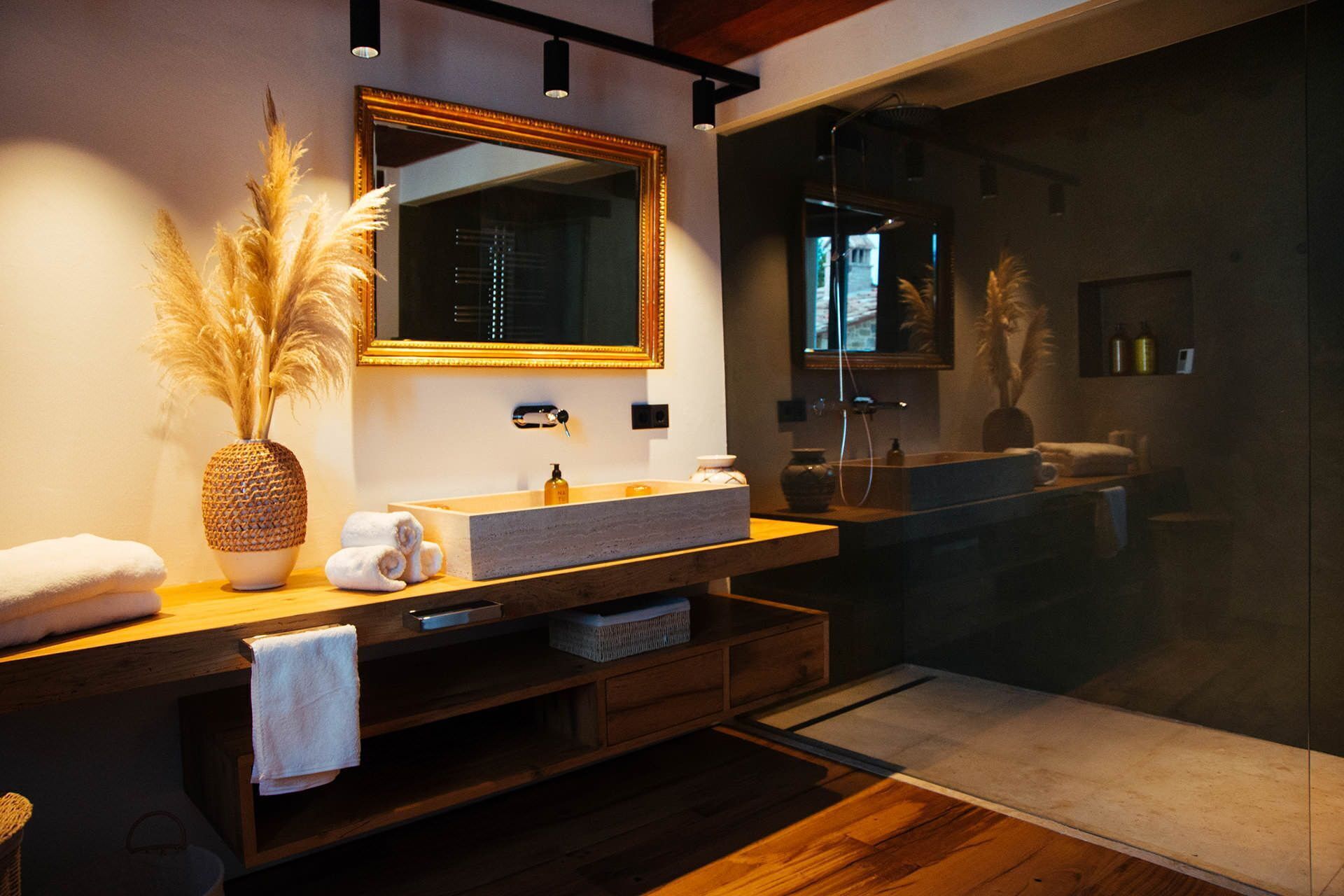 Un baño moderno con un espejo grande, un lavamanos de piedra y un mueble de tocador de madera.