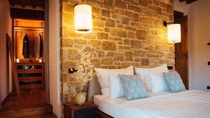 A bedroom with a stone wall, a wooden bed frame, and a nightstand. - My Rental Homes - Villa Torre del Chianti with hited pool, Gym and wellness center (Radda In Chianti)