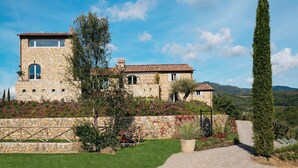 A stone building with a tower, surrounded by a well-maintained garden and a clear sky. - My Rental Homes - Villa Torre del Chianti with hited pool, Gym and wellness center (Radda In Chianti)