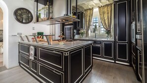 A modern kitchen with a central island, black cabinetry, and a large clock on the wall. - My Rental Homes - Villa Chianti with private pool, SPA and Gym (Tavarnelle Val Di Pesa)