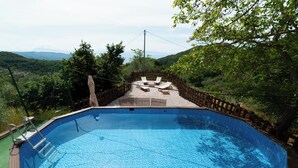 Una piscina amb un solàrium de fusta, gandules i vistes al paisatge circumdant.