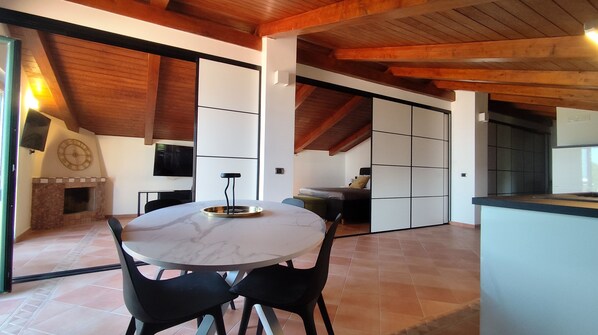 Un interior moderno con una mesa redonda de comedor, sillas negras, una chimenea y un televisor montado en la pared.