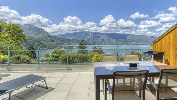 Una terraza con mesa y sillas con vistas a un lago y montañas.