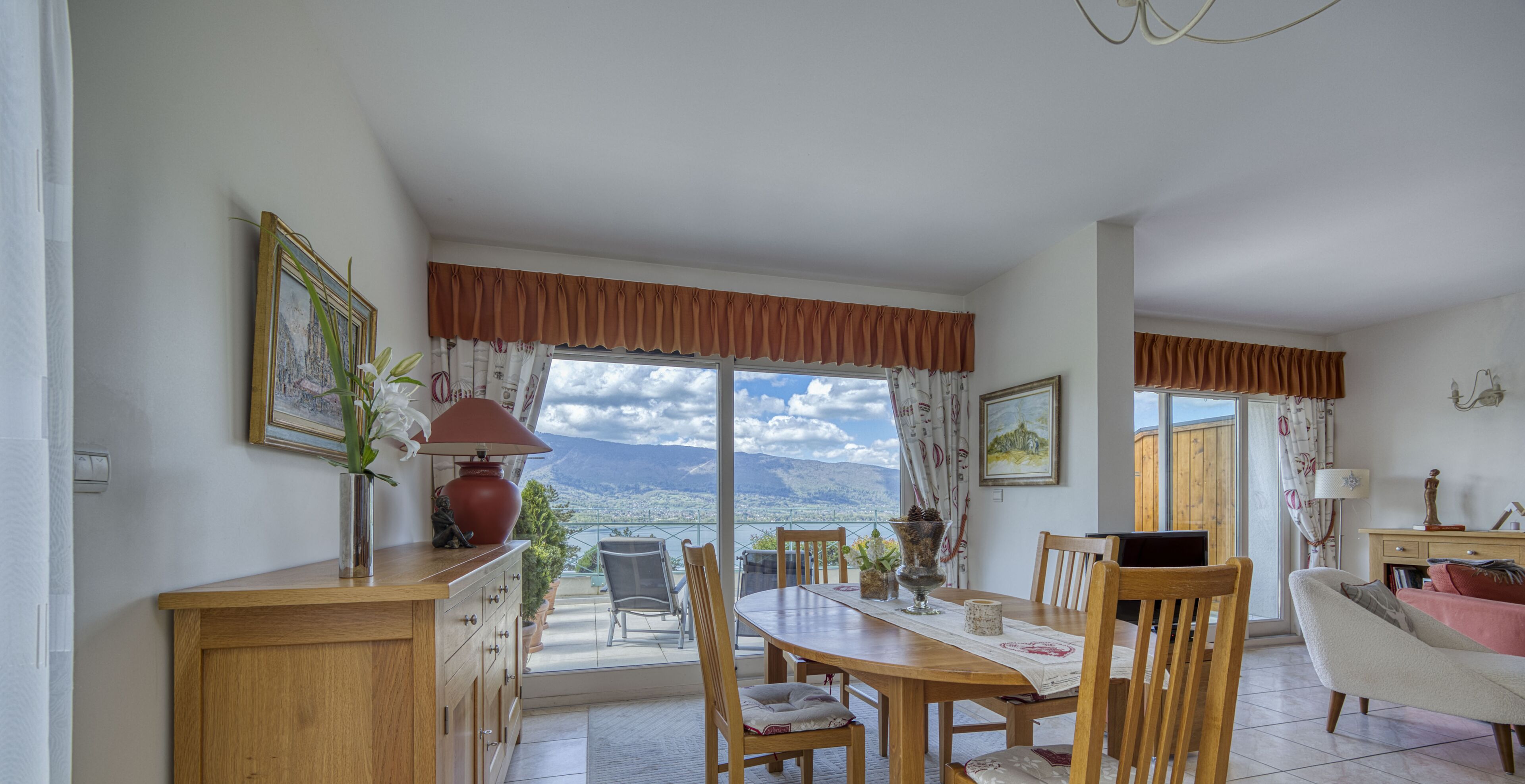 Un comedor con vistas a montañas, muebles de madera y un amplio ventanal con cortinas.