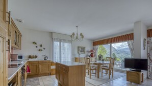 Una cocina amplia con armarios de madera, un comedor con mesa y sillas, un televisor y un gran ventanal con vistas a la montaña.