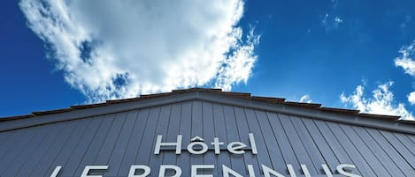 Señal de hotel con el nombre 'Hotel Le Brennus' sobre un cielo azul despejado con nubes.