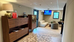 Een moderne hotellobby met een houten receptiebalie, een vloer met patroon, een bank, een televisiescherm en een wandairconditioner.