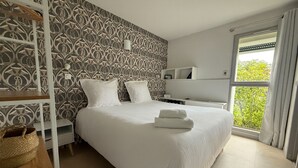 Een keurig opgemaakte slaapkamer met een groot bed, twee nachtkastjes, een garderobe en een raam met gordijnen.