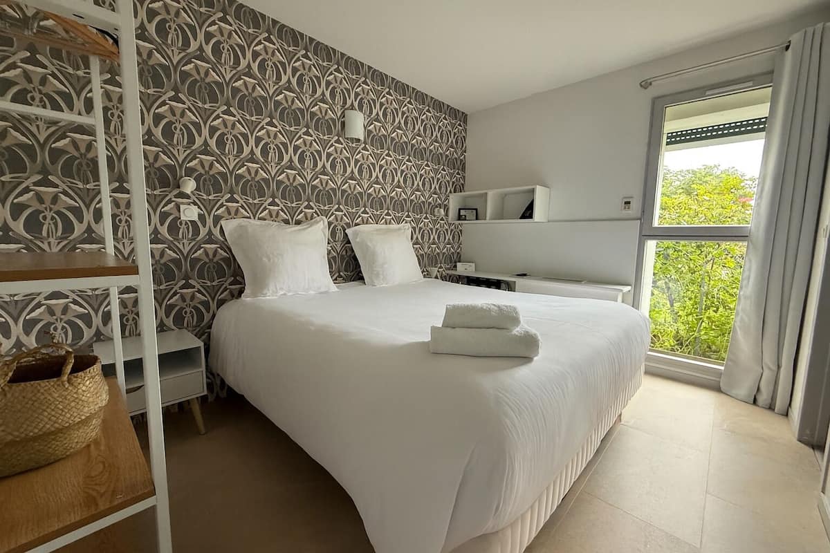 Een keurig opgemaakte slaapkamer met een groot bed, twee nachtkastjes, een garderobe en een raam met gordijnen.