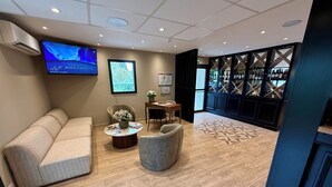 Een hotelhal met een bank, fauteuils, een bijzettafeltje met tijdschriften, een tv waarop een kaart wordt getoond en een wijnrekken.