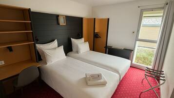 Quarto de hotel com duas camas, um guarda-roupa, uma escrivaninha e uma janela com persianas.