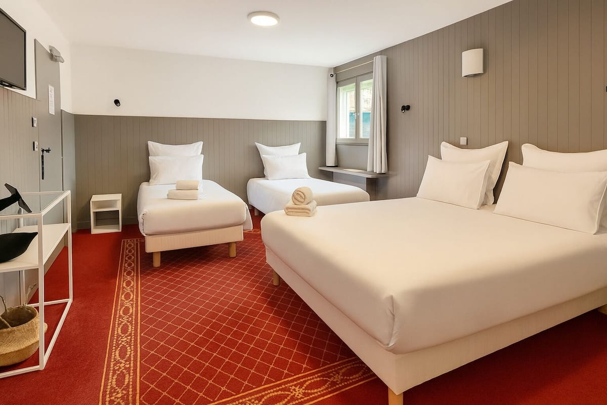 Hotelkamer met twee eenpersoonsbedden en een tweepersoonsbed, een rood tapijt met patroon, een klein nachtkastje en een tv aan de muur.