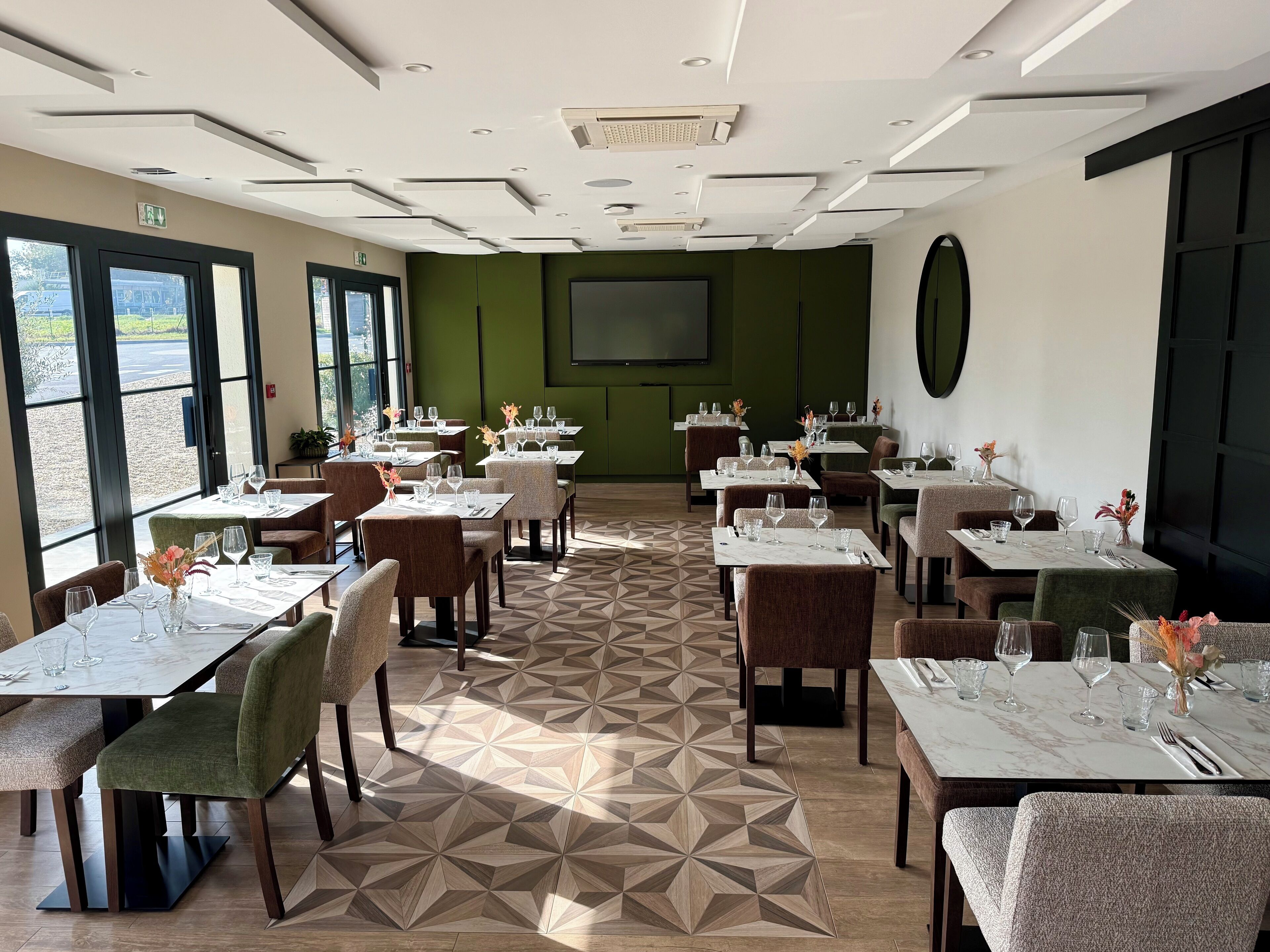 Un restaurant avec de nombreuses tables dressées pour le service, un grand écran fixé au mur et une vue par les fenêtres.