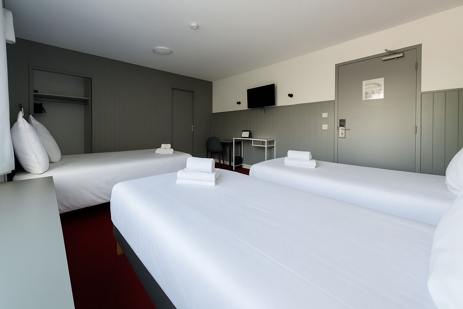 Een hotelkamer met twee bedden, een bureau, een stoel, een televisie en een kledingkast.