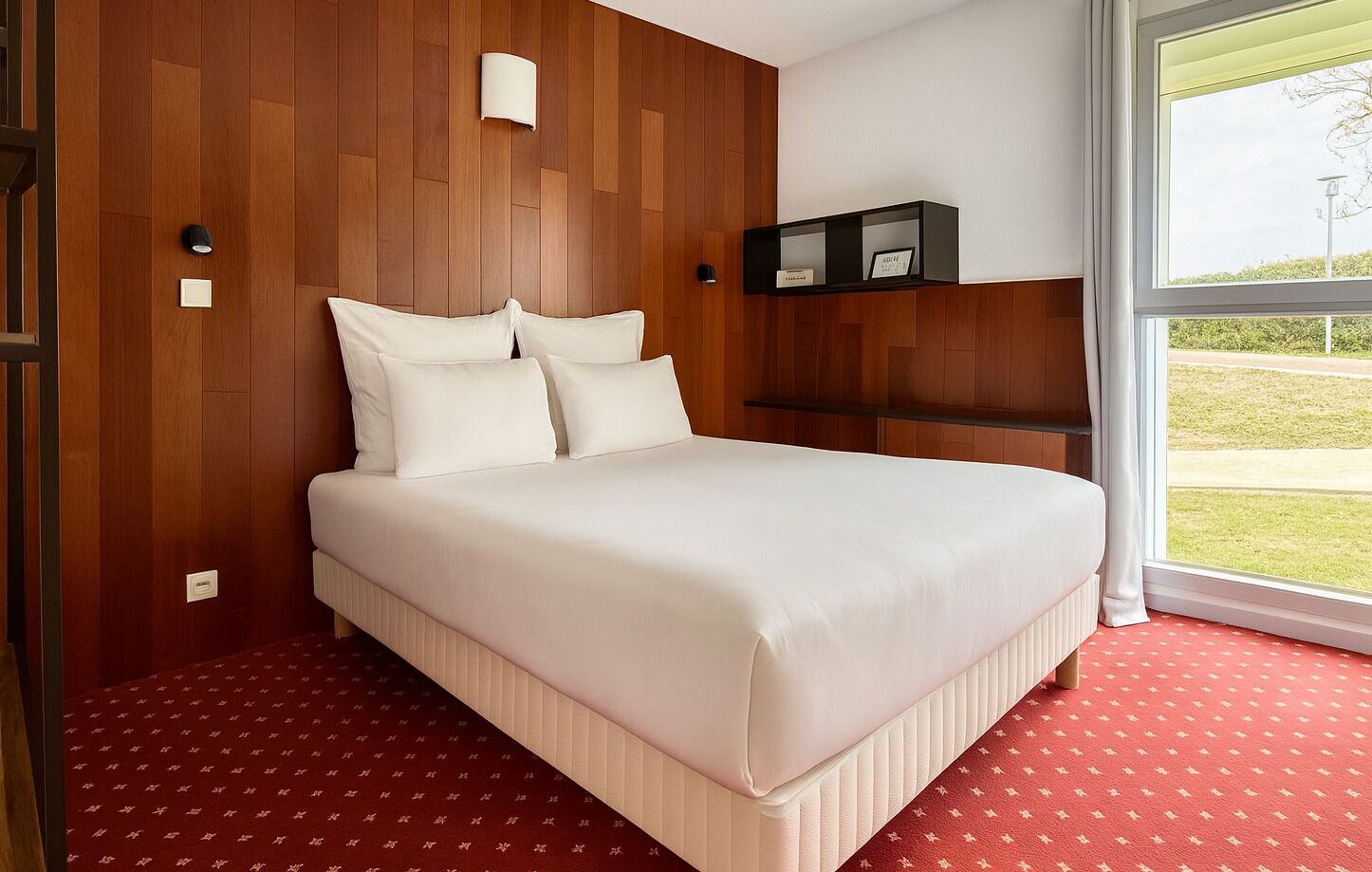 Hotelkamer met een groot bed, houten paneelwanden, een klein plankje en een raam met uitzicht op de omgeving.