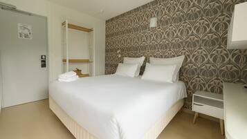 Una habitación de hotel con una cama bien hecha, una mesita de noche y un armario.
