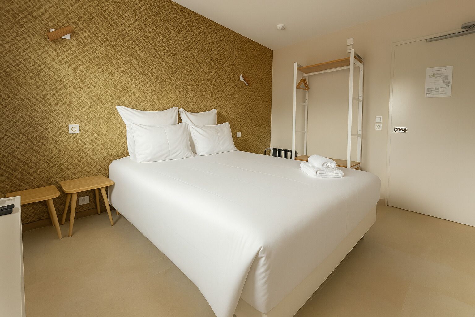 Habitación de hotel ordenada con una cama grande, una mesita de noche, una silla, un espejo y un armario.