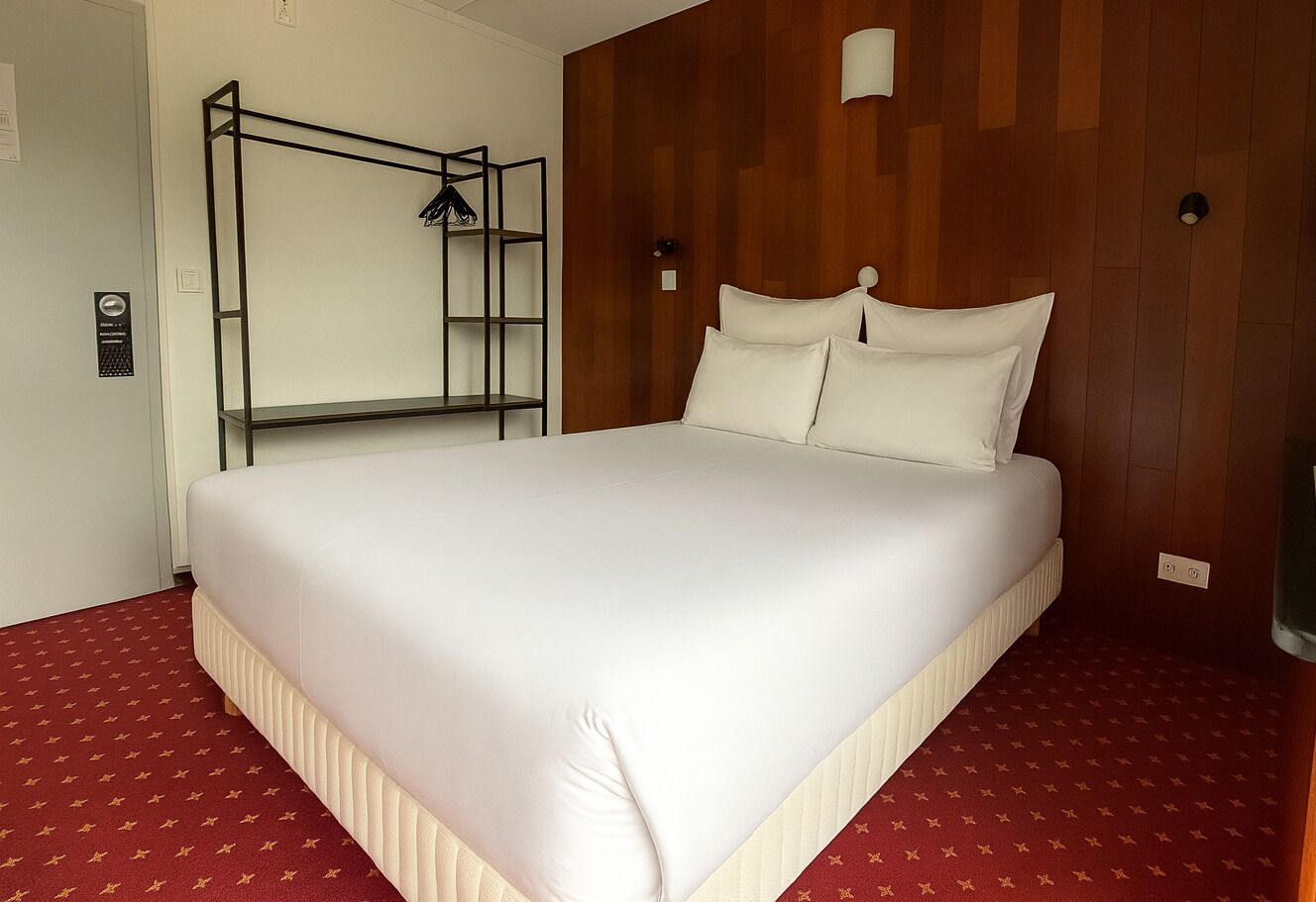 Una camera d'albergo con un letto grande, un pannello parete in legno e un tappeto rosso.