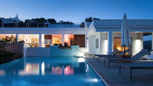 Un espace piscine moderne avec une terrasse en bois, des chaises longues et un mur en pierre.