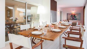 Un espace repas avec une longue table en bois, dressée pour six personnes, entourée de chaises blanches.