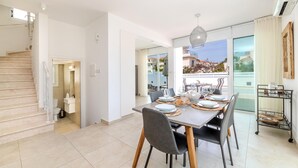 A modern dining area with a table set for four, a staircase, and a view of the outside. - Green Bay Villa #14 (Paralimni)