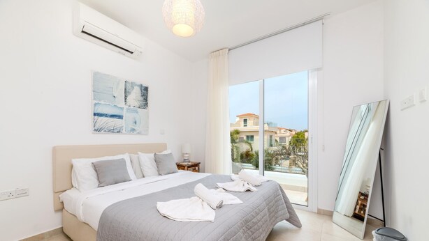 A modern hotel room with a large bed, a view of the city, and a balcony. - Green Bay Villa #14 (Paralimni)