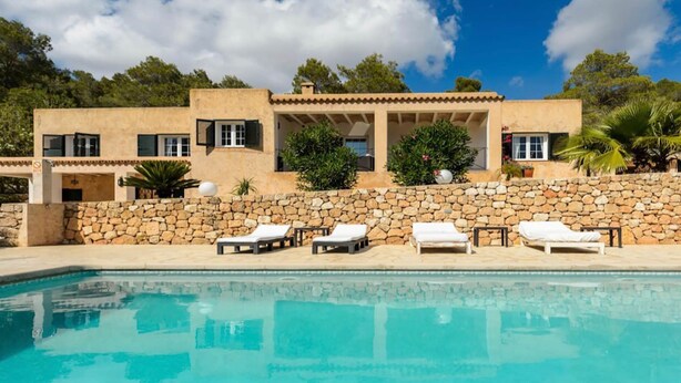 Une villa moderne dotée d’un mur en pierre, d’une piscine et d’un espace salon extérieur.