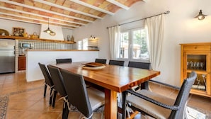 Un grand espace à manger avec une table en bois et des chaises en osier, une cuisine avec un dosseret carrelé et un ventilateur de plafond.