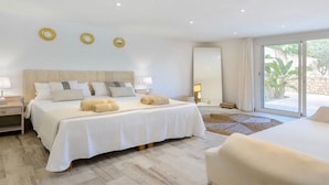 Une chambre moderne avec un grand lit, deux tables de chevet et une vue sur un jardin, accessible par une porte-fenêtre coulissante.