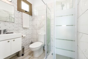 A modern bathroom with a white toilet, a glass-enclosed shower, a sink with a mirror, and a towel hanging on the wall. - Villa Levanda #40 (Paralimni)