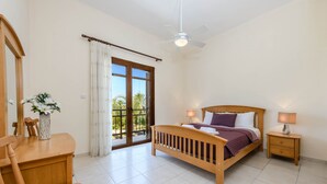 A bedroom with a bed, bedside tables, a desk, a chair, a ceiling fan, and a sliding glass door leading to a balcony. - Villa Greco Mare #5 (Paralimni)
