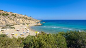 A beach with clear blue waters, sandy shore, and rocky hills in the background. - Villa Greco Mare #5 (Paralimni)
